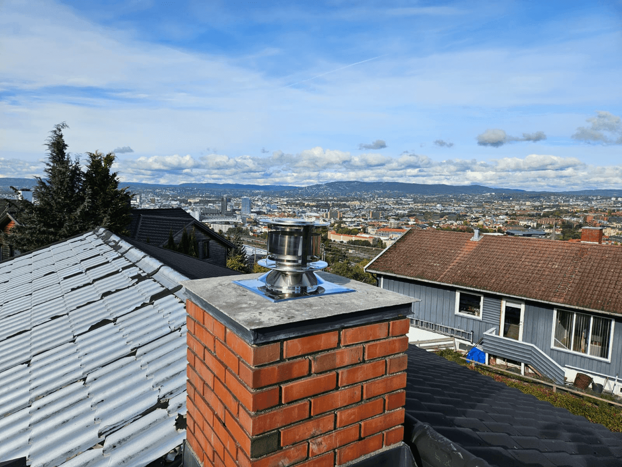 Et stålrør installeres i en mursteinskorstein under rehabilitering, med verktøy og utsikt over byen i bakgrunnen.